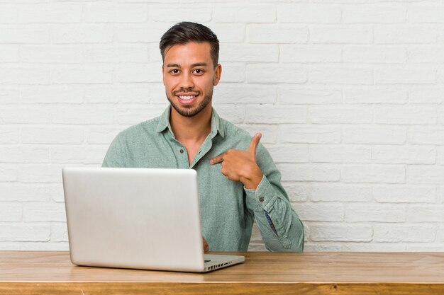 Jonge Filipijnse mensenzitting die met zijn laptop persoon werken die met de hand aan een ruimte van het overhemdsexemplaar richten, trots en zeker