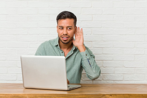 Jonge filipijnse mensenzitting die met zijn laptop werken die een roddel proberen te luisteren.