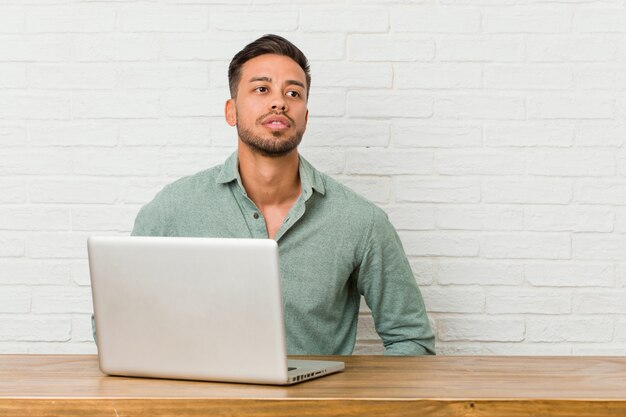 Jonge Filipijnse mensenzitting die met zijn laptop werken die zeker handen op heupen houden.