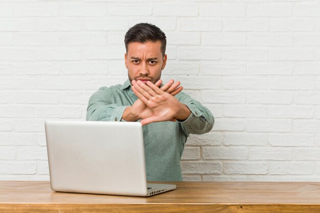 Jonge Filipijnse mensenzitting die met zijn laptop werkt die een ontkenningsgebaar doet