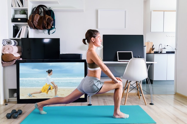 Foto jonge fit vrouw doet yoga stretching oefening binnen in de buurt van tv-scherm op isolatie bij haar thuis