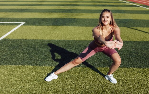 Jonge fit vrouw in sportkleding doet pre-training warming-up, lichaam strekken in het stadion. Gezond levensstijlconcept.