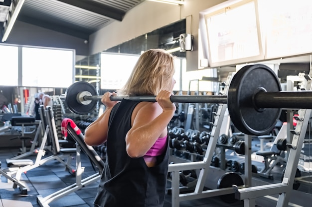 Jonge fit vrouw op de sportschool doet zware oefening. Vrouwelijke atleet in een fitnessruimte uit te werken met barbell