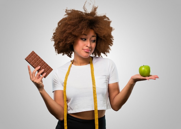 Jonge fitness afro vrouw kiezen tussen gezond eten of chocolade