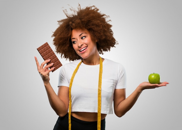 Jonge fitness afro vrouw kiezen tussen gezond eten of chocolade