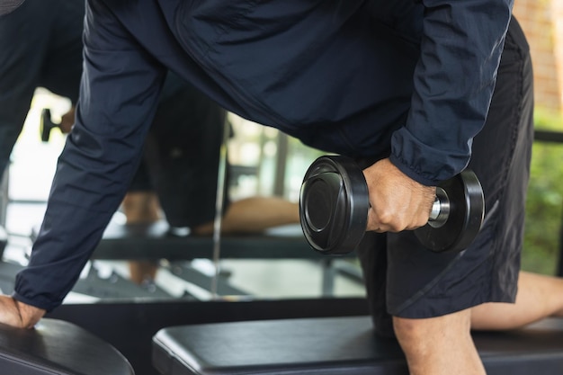 Foto jonge fitness man met halter in de sportschool. guy krachttraining dragen van sportkleding. aziatische man oefenen indoor sportschool opheffing halter. bodybuilder goede gezondheid