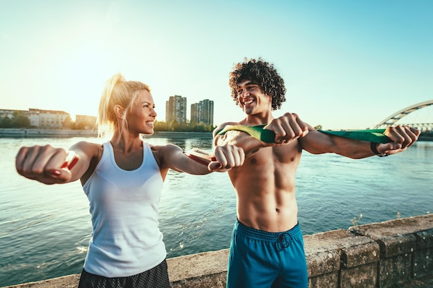 Jonge fitness paar doet training met rubberen band aan de rivier in een zonsondergang.