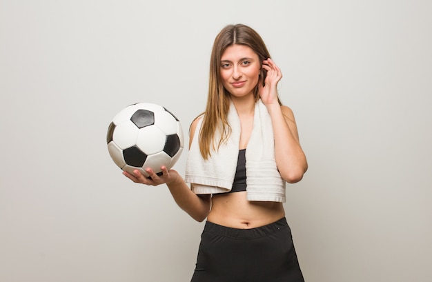 Jonge fitness Russische vrouw die oren behandelt met handen. Een voetbal vasthouden.