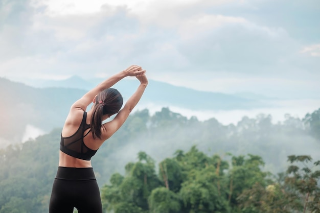 Jonge fitness vrouw in sportkleding lichaam uitrekken tegen uitzicht op de bergen, gezonde vrouw oefenen in de ochtend. Concepten voor training, welzijn en balans tussen werk en privé