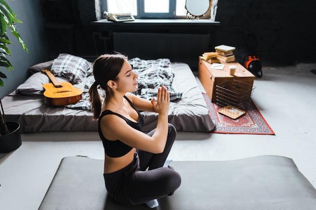 Jonge fitness vrouw mediteren, yoga binnenshuis thuis in de buurt van het bed doen