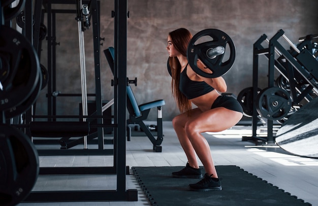 Jonge fitness vrouw met slank type lichaam doet oefeningen met behulp van barbell.