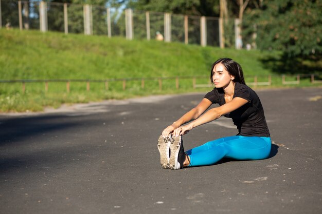 Jonge fitness vrouw runner doen stretching voor de training. Buiten geschoten met zonnestralen. Ruimte voor tekst