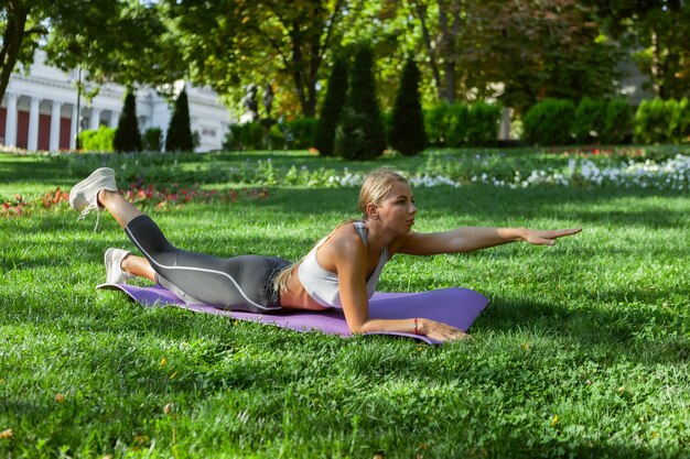 Jonge fitness vrouw uit te werken op yoga mat in het park buiten. Gezonde levensstijl