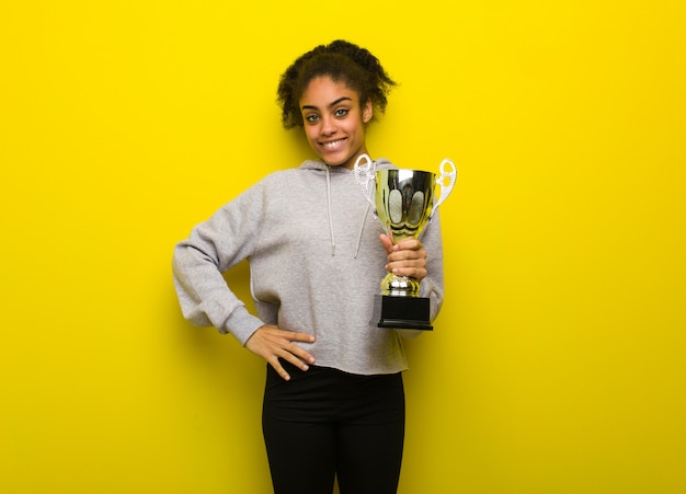 Jonge fitness zwarte vrouw met handen op de heupen. Met een trofee.