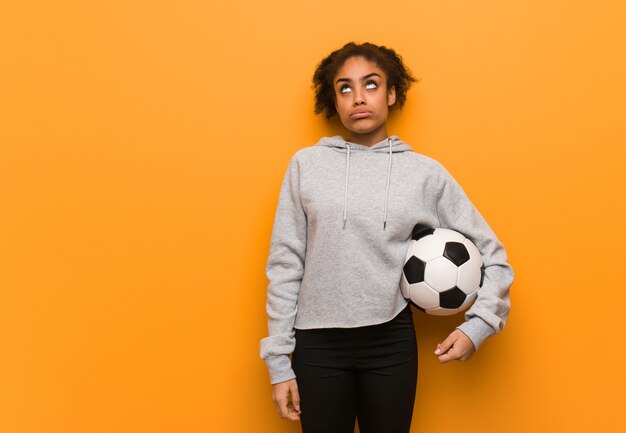 Jonge fitness zwarte vrouw moe en verveeld. Een voetbal vasthouden.