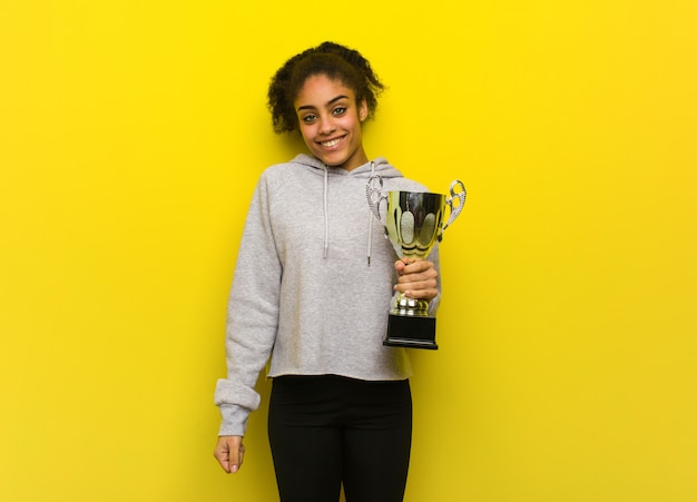 Jonge fitness zwarte vrouw vrolijk met een grote glimlach. Met een trofee.