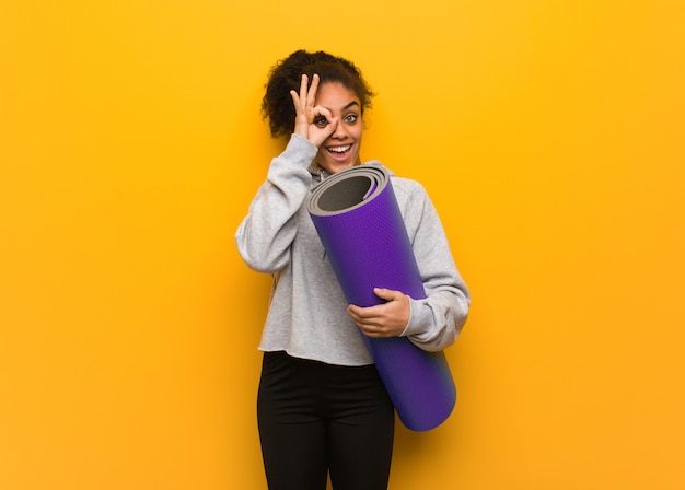 Jonge fitness zwarte vrouw zeker doen ok gebaar op oog. Een mat vasthouden.