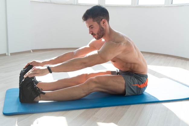 Jonge fitnessman strekt zich uit op de vloer