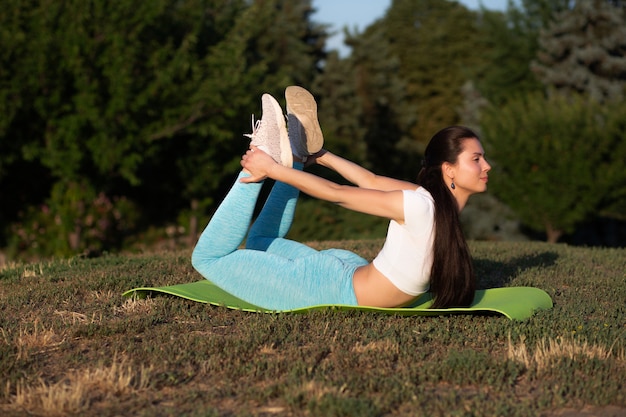 Jonge fitnessvrouw die sportkleding draagt die zich uitstrekt in het park bij zonsondergang