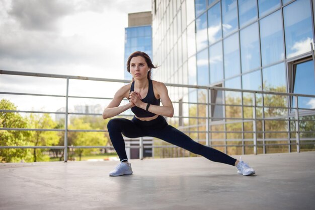 Jonge fitnessvrouw doet opwarm-oefeningen in de buurt van de stad en bouwt een gezonde levensstijl