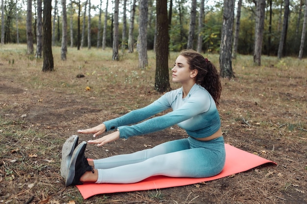Jonge fitnessvrouw oefent op de mat in het bos Gezonde levensstijl Outdoor workout