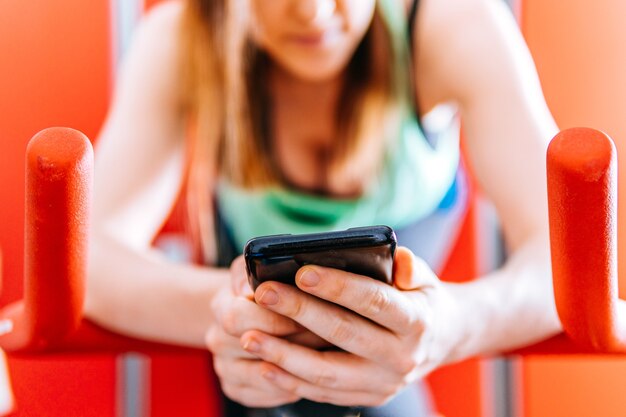 Jonge fitte atleetvrouw die naar smartphone kijkt tijdens het fietsen indor spinnen