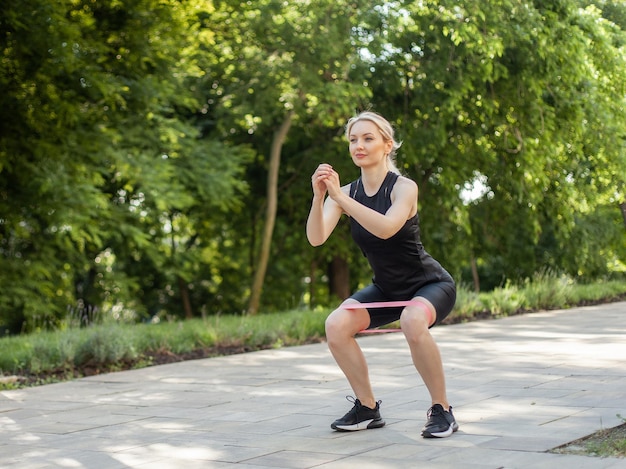 Jonge fitte blonde vrouw kraakpanden met fitness rubberen band in park