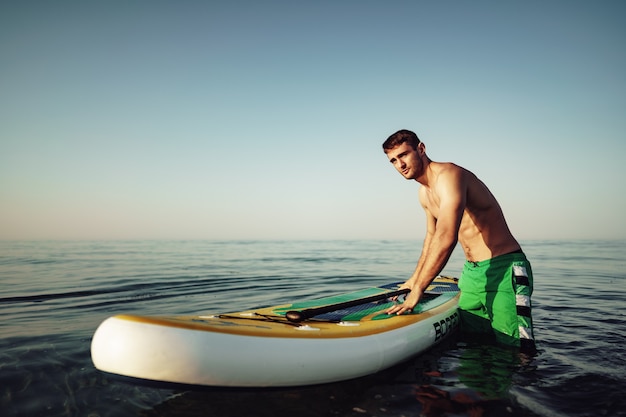 Jonge fitte man op paddleboard drijvend op het meer