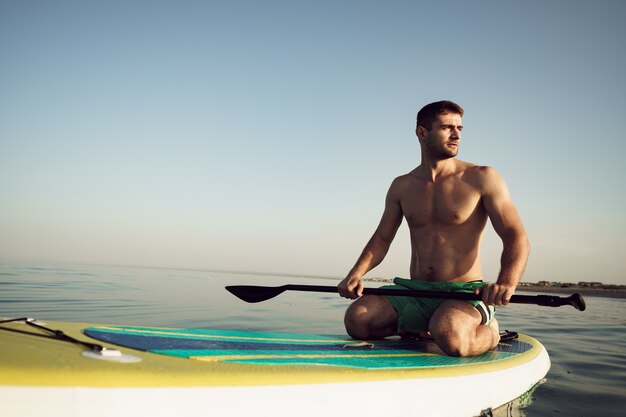 Jonge fitte man op paddleboard drijvend op het meer