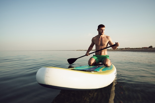 Jonge fitte man op paddleboard drijvend op het meer