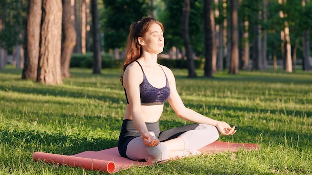 Jonge fitte vrouw mediteert in een zonnig park op een yogamat