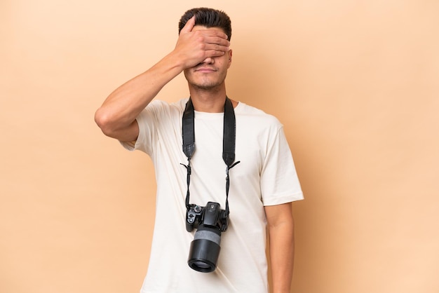 Jonge fotograaf blanke man geïsoleerd op beige achtergrond die ogen bedekt met handen Wil je iets niet zien?