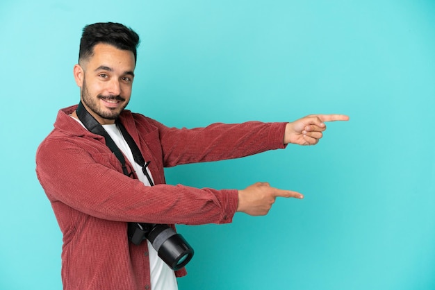 Jonge fotograaf blanke man geïsoleerd op blauwe achtergrond wijzende vinger naar de zijkant en presenteren van een product