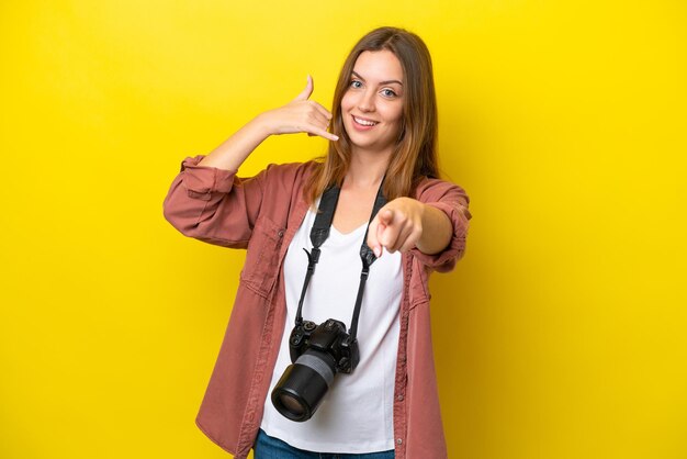 Jonge fotograaf blanke vrouw geïsoleerd op gele achtergrond telefoon gebaar maken en naar voren wijzen