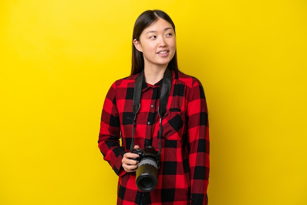 Jonge fotograaf Chinese vrouw geïsoleerd op gele achtergrond gelukkig en glimlachend