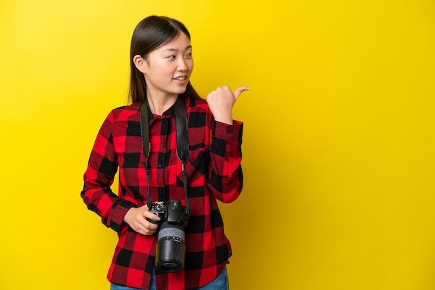 Jonge fotograaf Chinese vrouw geïsoleerd op gele achtergrond wijzend naar de zijkant om een product te presenteren