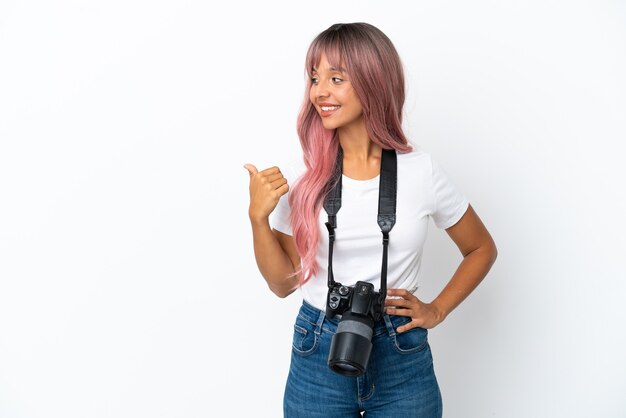 Jonge fotograaf gemengd ras vrouw met roze haar geïsoleerd op een witte achtergrond wijzend naar de zijkant om een product te presenteren