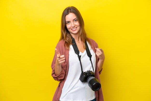 Jonge fotograaf kaukasische vrouw geïsoleerd op een gele achtergrond die naar voren wijst en glimlacht