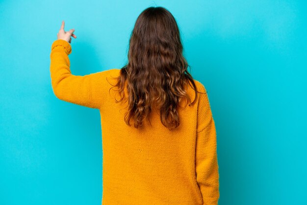 Jonge fotograaf vrouw geïsoleerd op blauwe achtergrond terug te wijzen met de wijsvinger