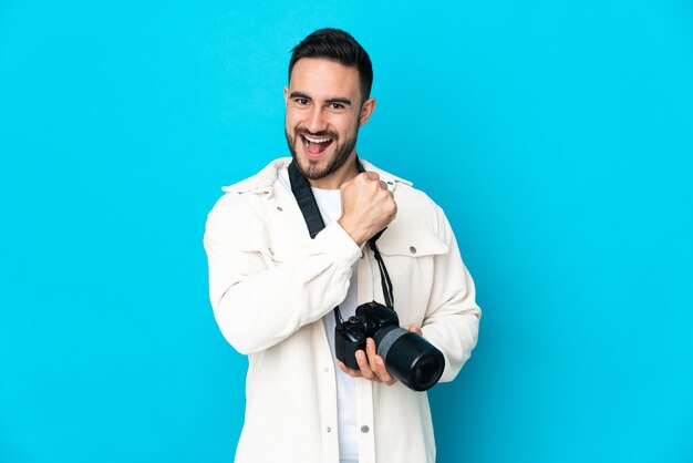 Jonge fotograafmens die op blauwe achtergrond wordt geïsoleerd die een overwinning viert