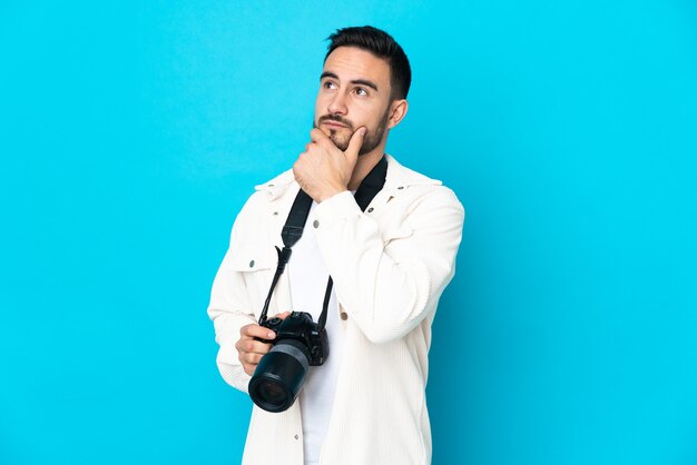 Jonge fotograafmens die op blauwe achtergrond wordt geïsoleerd die twijfels heeft