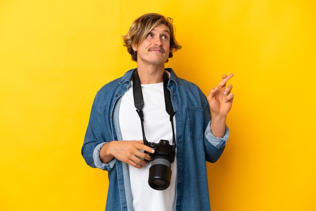 Jonge fotograafmens die op gele muur met vingers wordt geïsoleerd die en het beste wensen