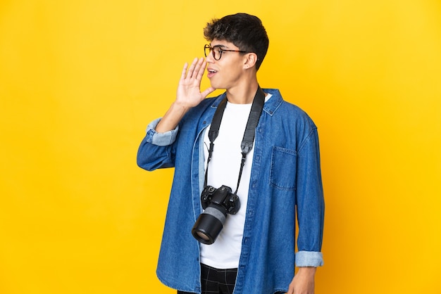 Jonge fotograafmens op geïsoleerd geel schreeuwend met wijd open mond aan de zijkant