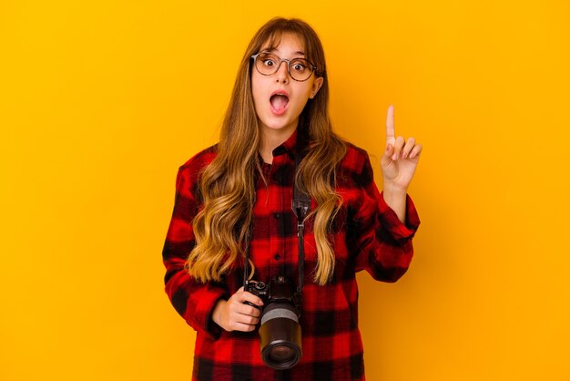 Jonge fotograafvrouw die op gele muur wordt geïsoleerd die een idee, inspiratieconcept heeft