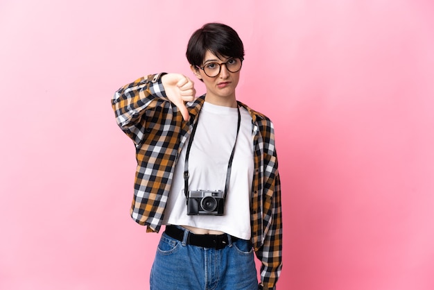 Jonge fotograafvrouw op roze die duim met negatieve uitdrukking toont