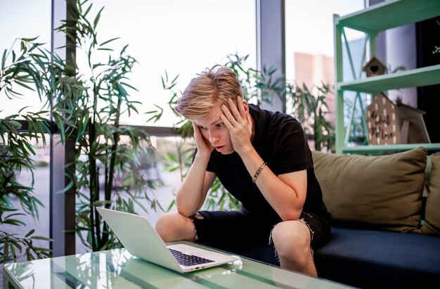 Foto jonge freelance man die op een laptop werkt terwijl hij aan een tafel in de cafetaria zit