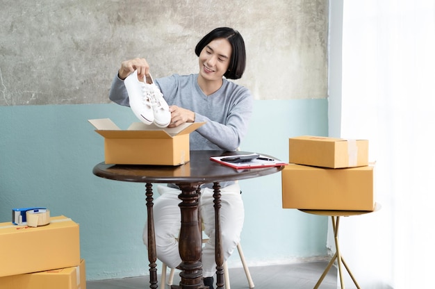 Jonge freelancer Aziatische man zaken online tijdens het verpakken van schoenenproduct aan klant met karton