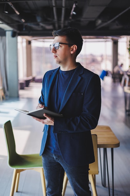 Jonge freelancer man aan het werk in een café met een notitieblok een zakenman met een notitieblok een man in een jas en bril