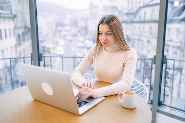 Jonge freelancer-vrouw gebruikt een laptop aan een cafétafel Ernstige vrouw surft op internet of studeert terwijl ze een computer gebruikt