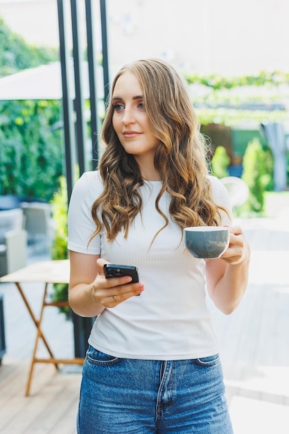 Jonge freelancer vrouw in casual kleding koffie drinken en praten aan de telefoon werken op een groen terras kijken naar een scherm en werken aan een project op afstand van het werk in een café